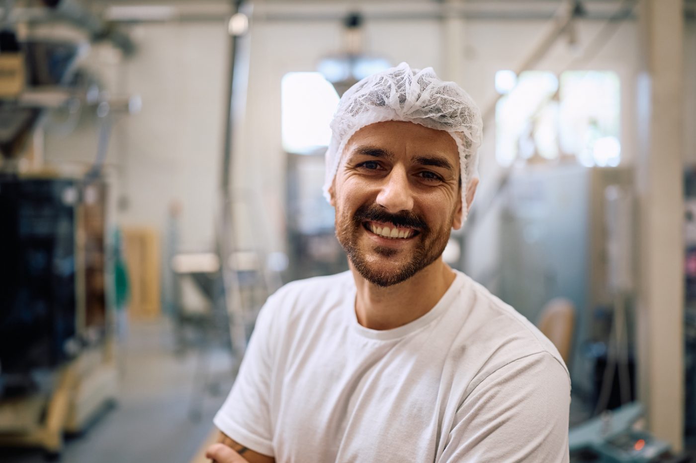 Muncitor zâmbitor cu bonetă de protecție într-o fabrică de producție alimentară